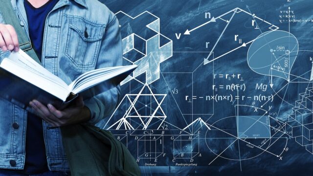数学の公式が書かれている黒板の前で男が本を読んでる